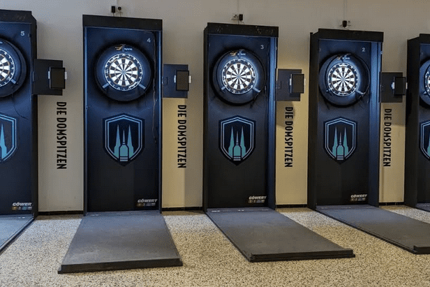 Sechs Dartscheiben an Wänden mit schwarzem Design, beschriftet mit „DIE DOMSPITZEN“, auf einem glatten Boden.